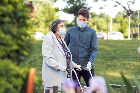Young man helps elderly woman walk with a walker during COVID-19