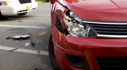 Smashed passenger side front end of a red vehicle with a police car in the background and a hubcap on the ground