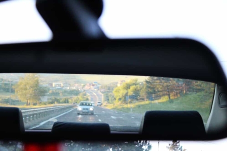 Close up of a car's rear view mirror with a car following behind