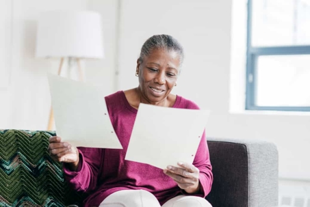 Older woman looks over paperwork while sitting on a couch in a bright room