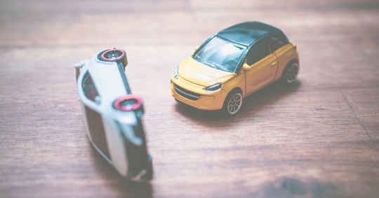 two toy cars, one toppled over like a car accident